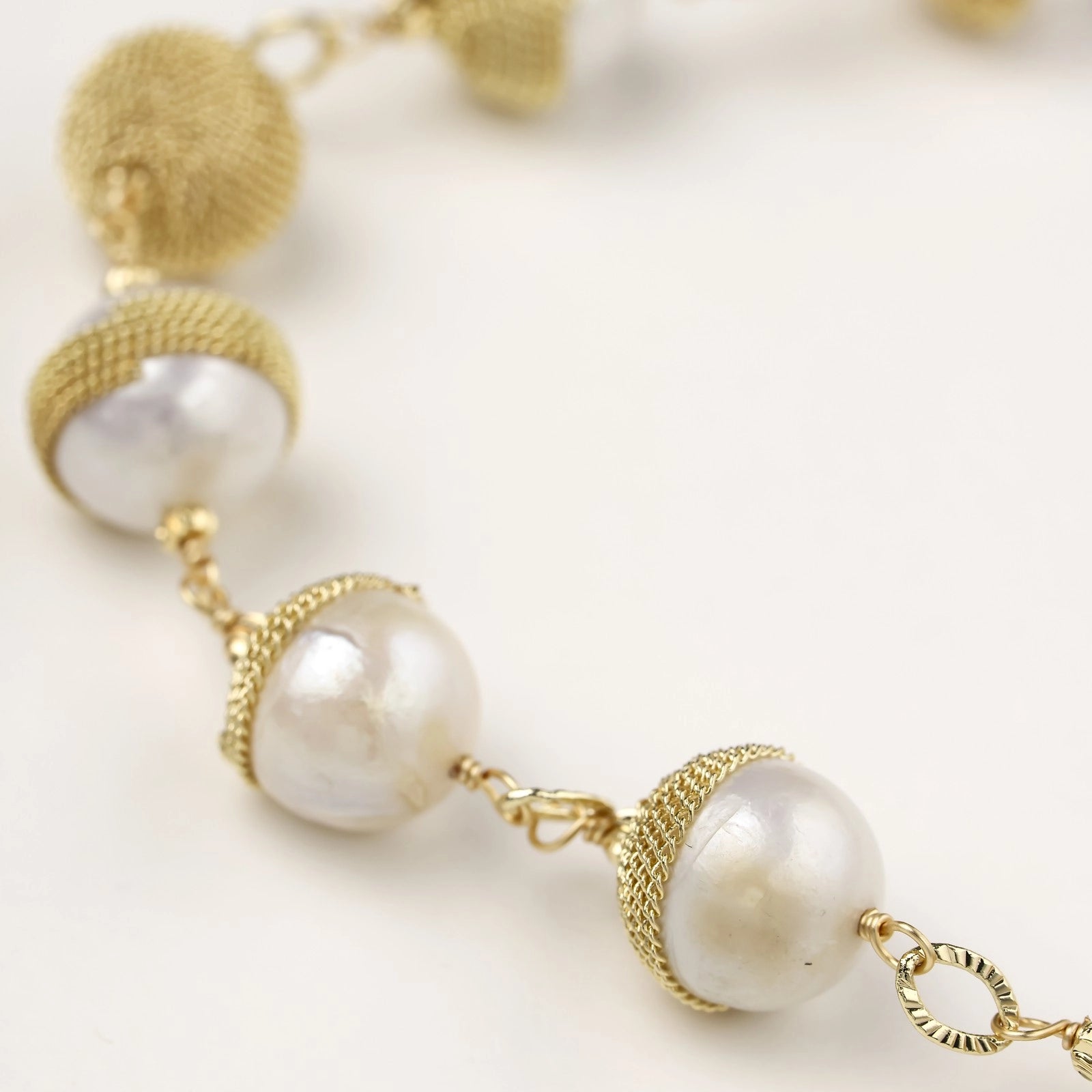 Adjustable bracelet featuring baroque pearls wrapped in gold mesh wire with delicate chain links on cream background.