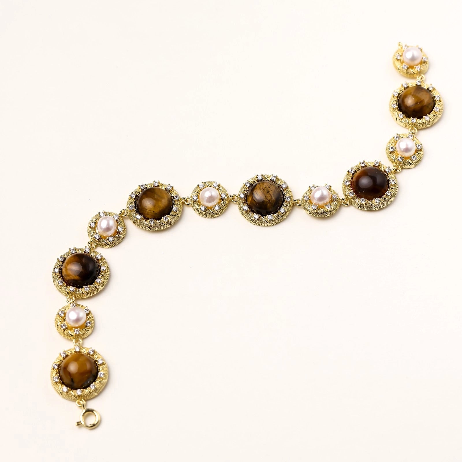 Ornate gold-plated bracelet with alternating brown tiger's eye stones and white freshwater pearls in crystal-accented settings