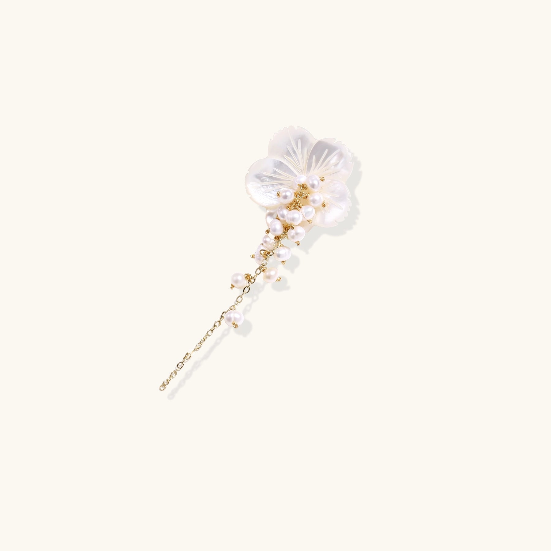 Delicate hair pin featuring translucent shell flower with cascading freshwater pearls on gold chain against cream background.