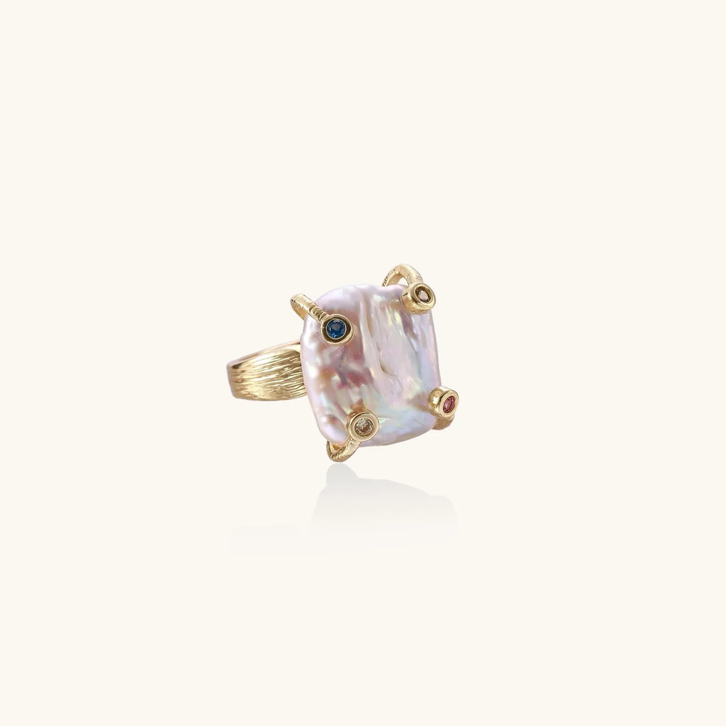 Gold-plated ring featuring large baroque freshwater pearl with small colorful gemstone accents on textured band