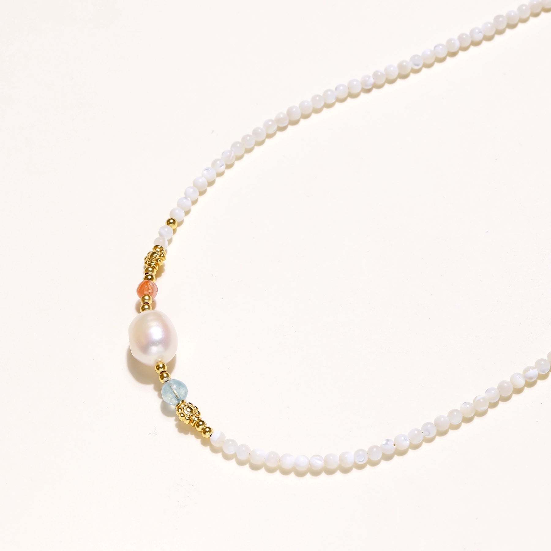 Delicate white beaded necklace with central freshwater pearl and gold-toned emerald accents on white background.