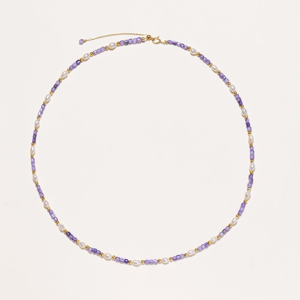 Delicate beaded necklace with alternating purple zirconia stones, white freshwater pearls, and gold-plated spacers on cream background.