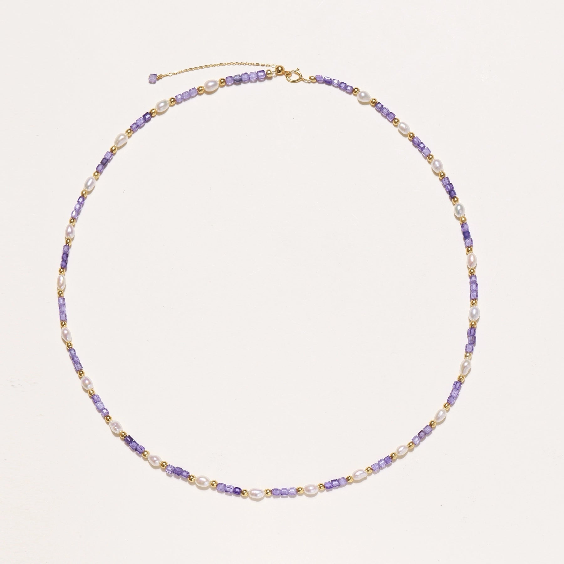 Delicate beaded necklace with alternating purple zirconia stones, white freshwater pearls, and gold-plated spacers on cream background.