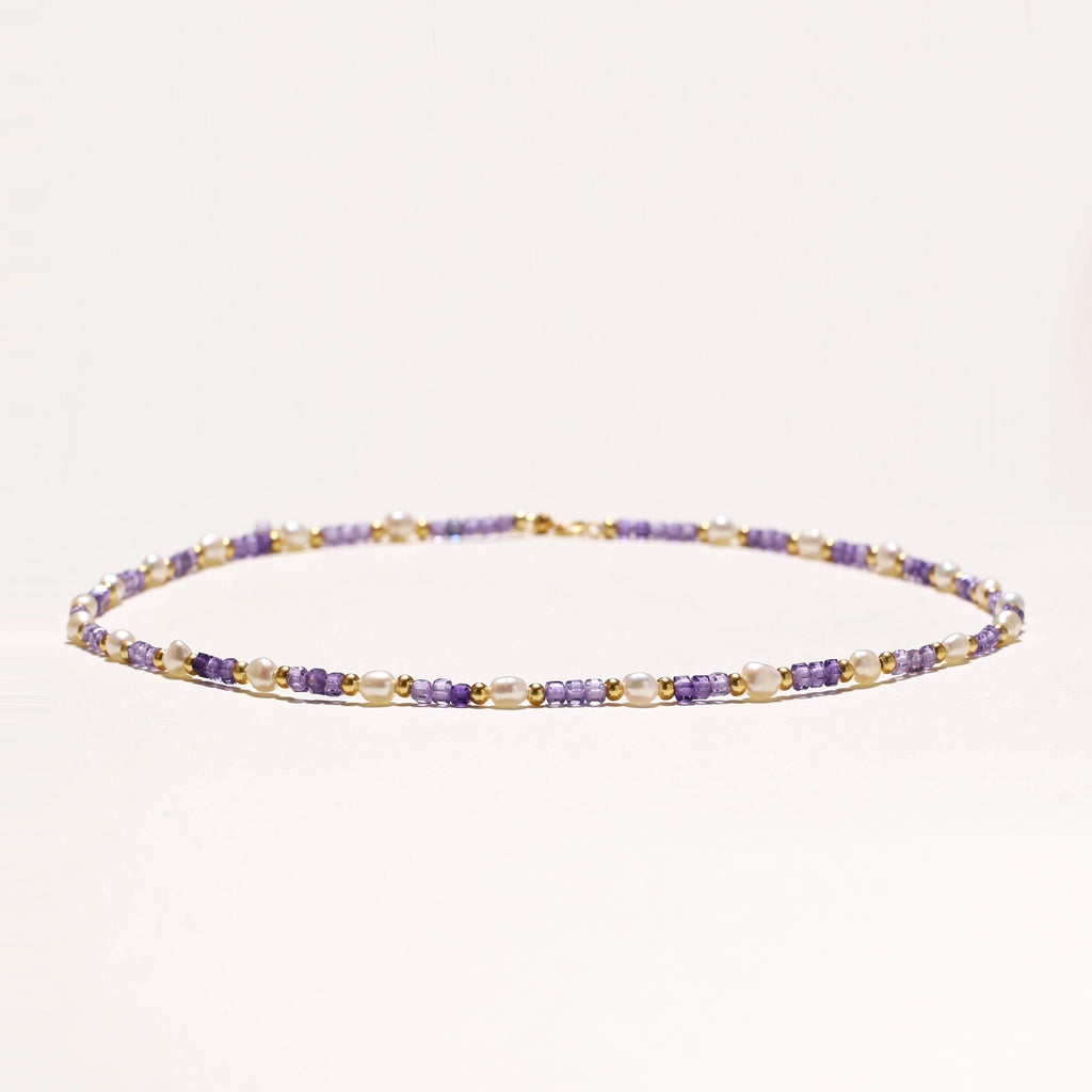 Delicate beaded necklace with alternating purple zirconia stones, white freshwater pearls, and gold-plated spacers on cream background.