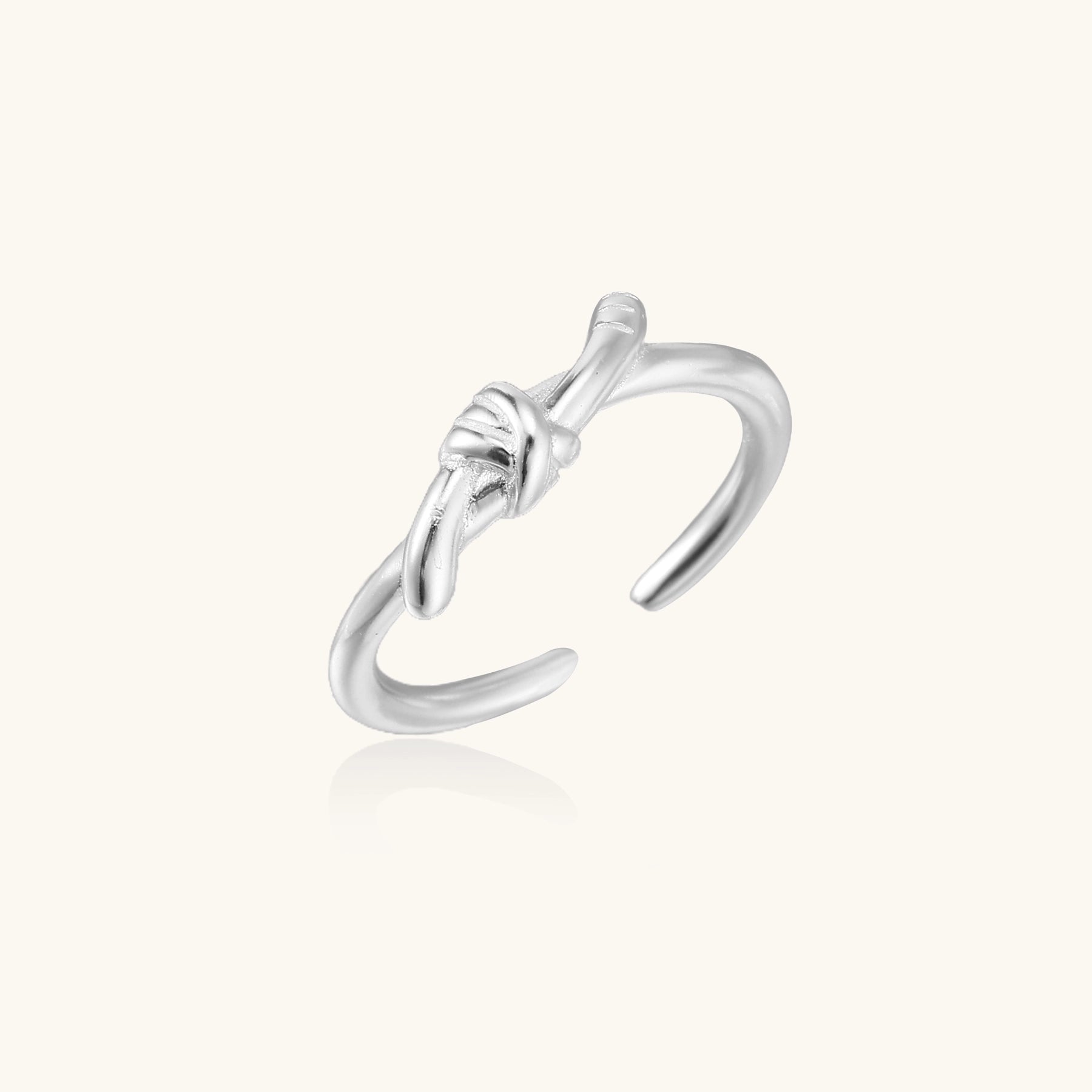 Delicate sterling silver ring with geometric knot design on white background, showcasing adjustable open band.
