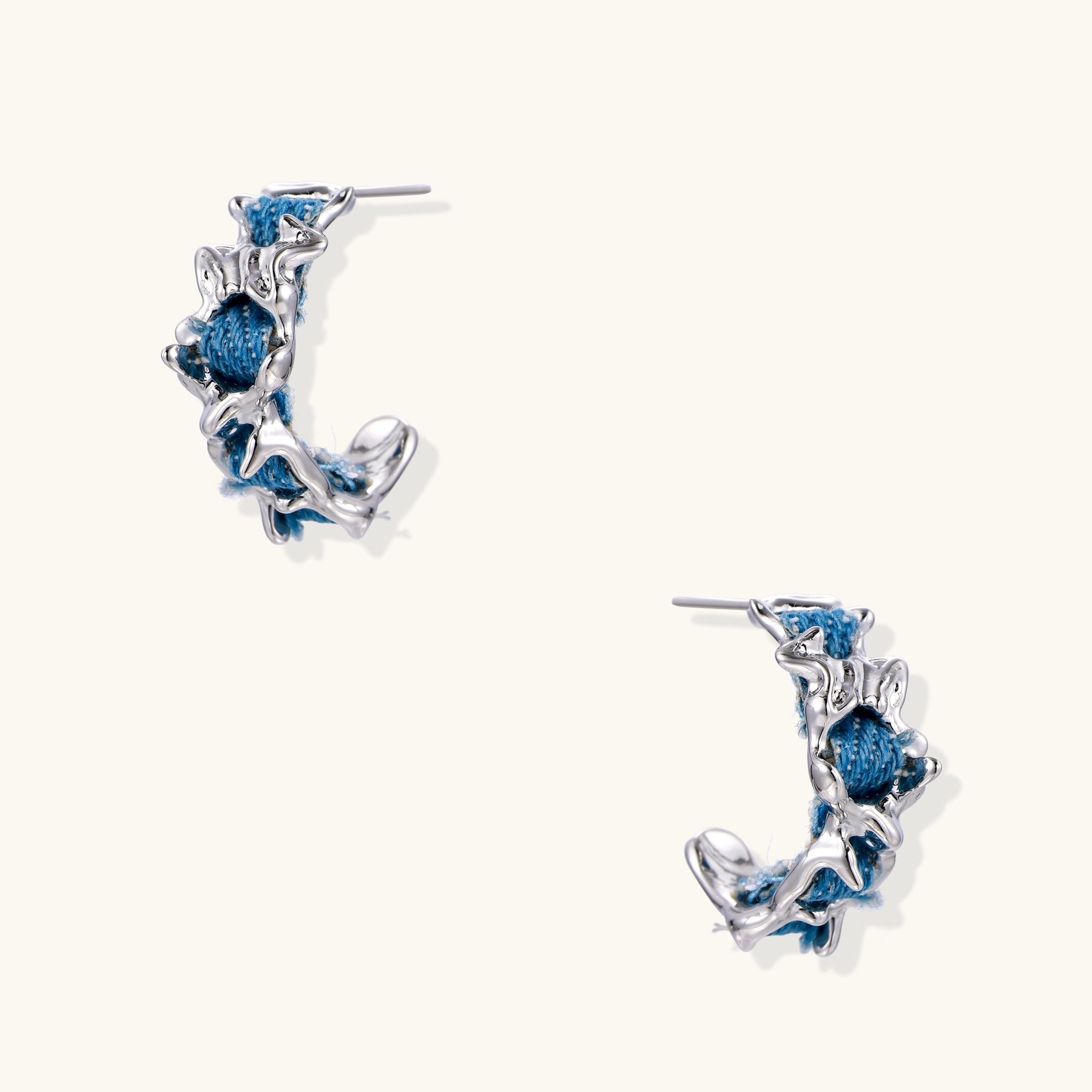 Crescent-shaped gold-plated hoop earrings with blue crystals set in organic vine-like metalwork on white background.