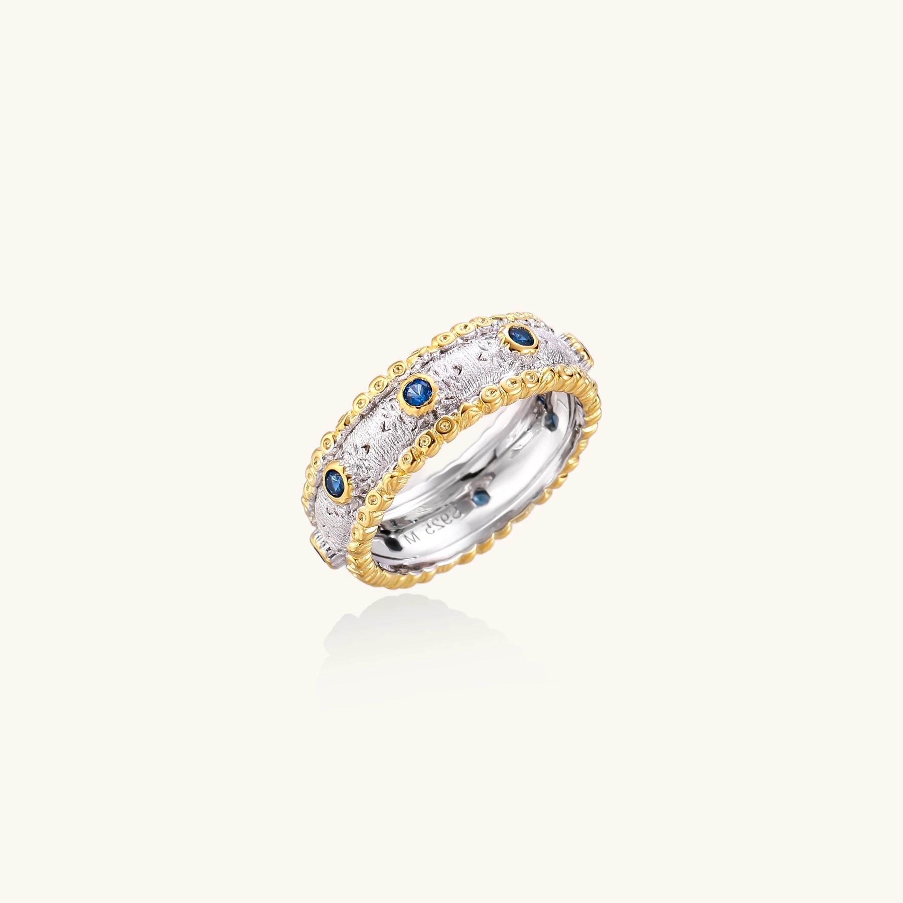 Sterling silver ring with brushed center band, blue zirconia stones, and 24k gold-plated decorative borders.