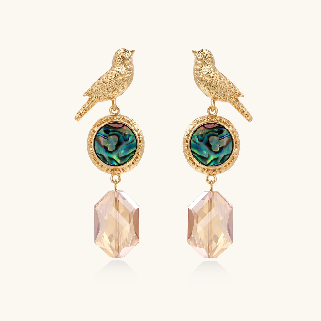 Gold-plated bird dangle earrings with iridescent abalone shell discs and champagne crystal drops on white background.