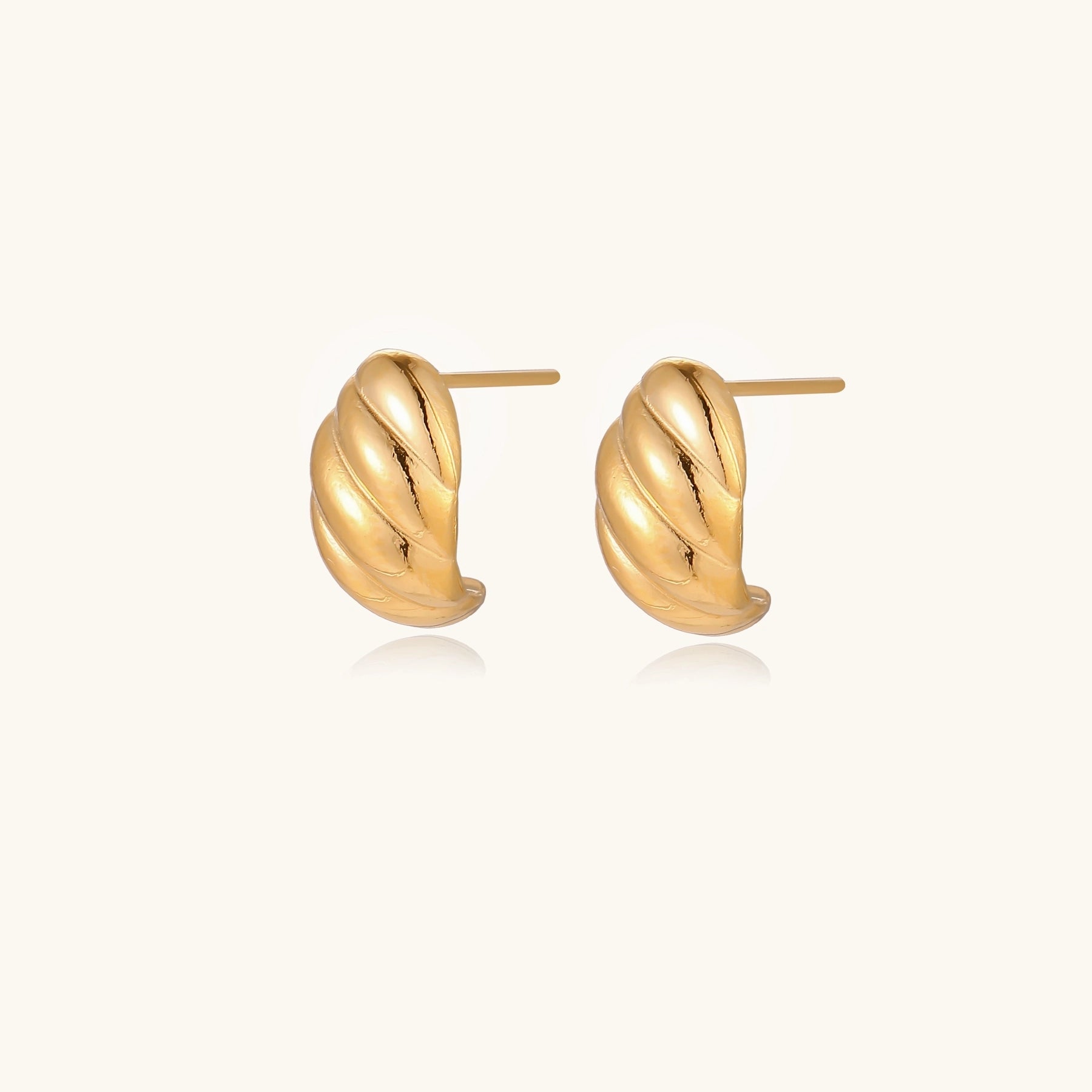Pair of gold-plated twisted stud earrings with sculptural spiral design displaying elegant curved ridges on cream background.
