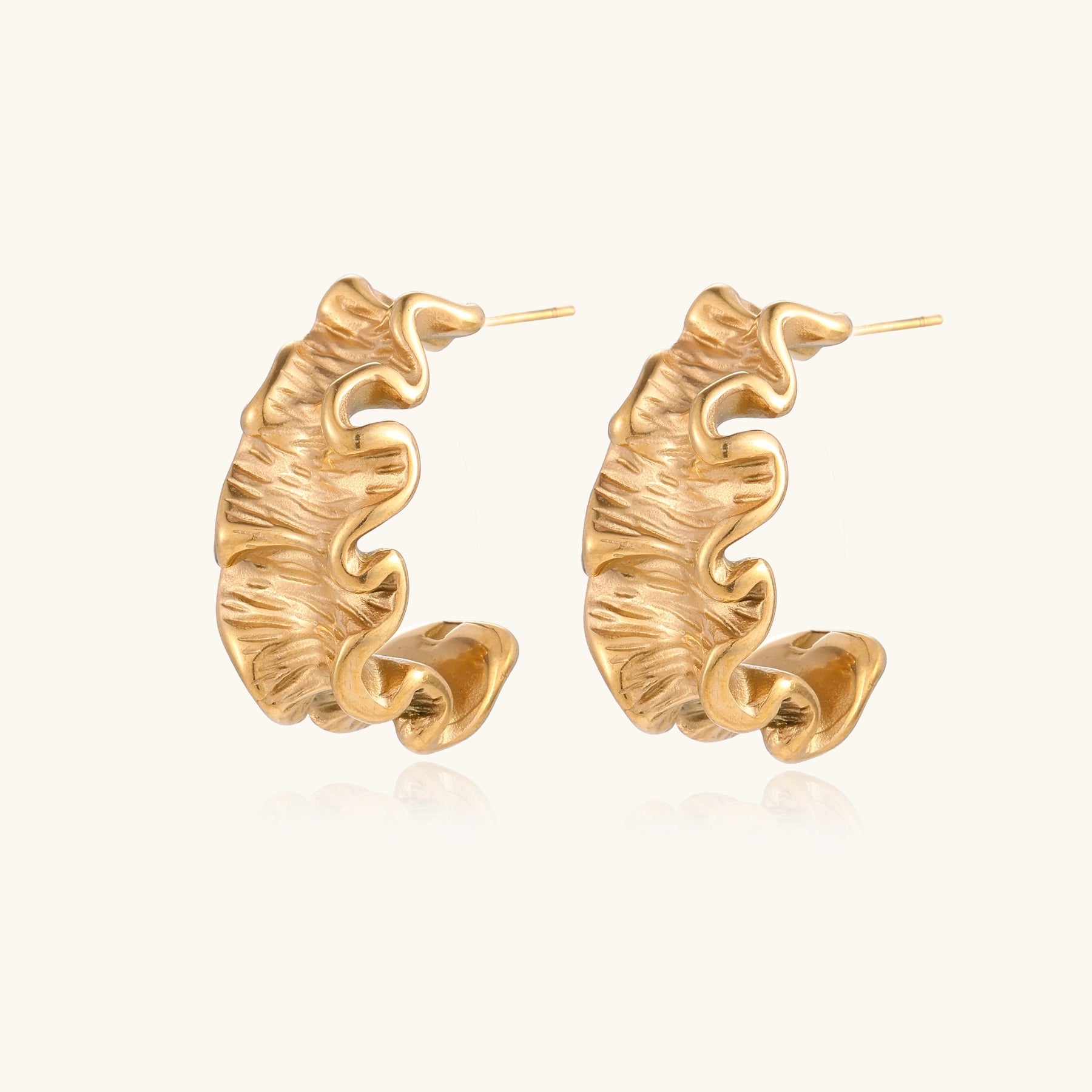 Textured gold-plated hoop earrings with wavy sculptural ridges displayed against a neutral background.