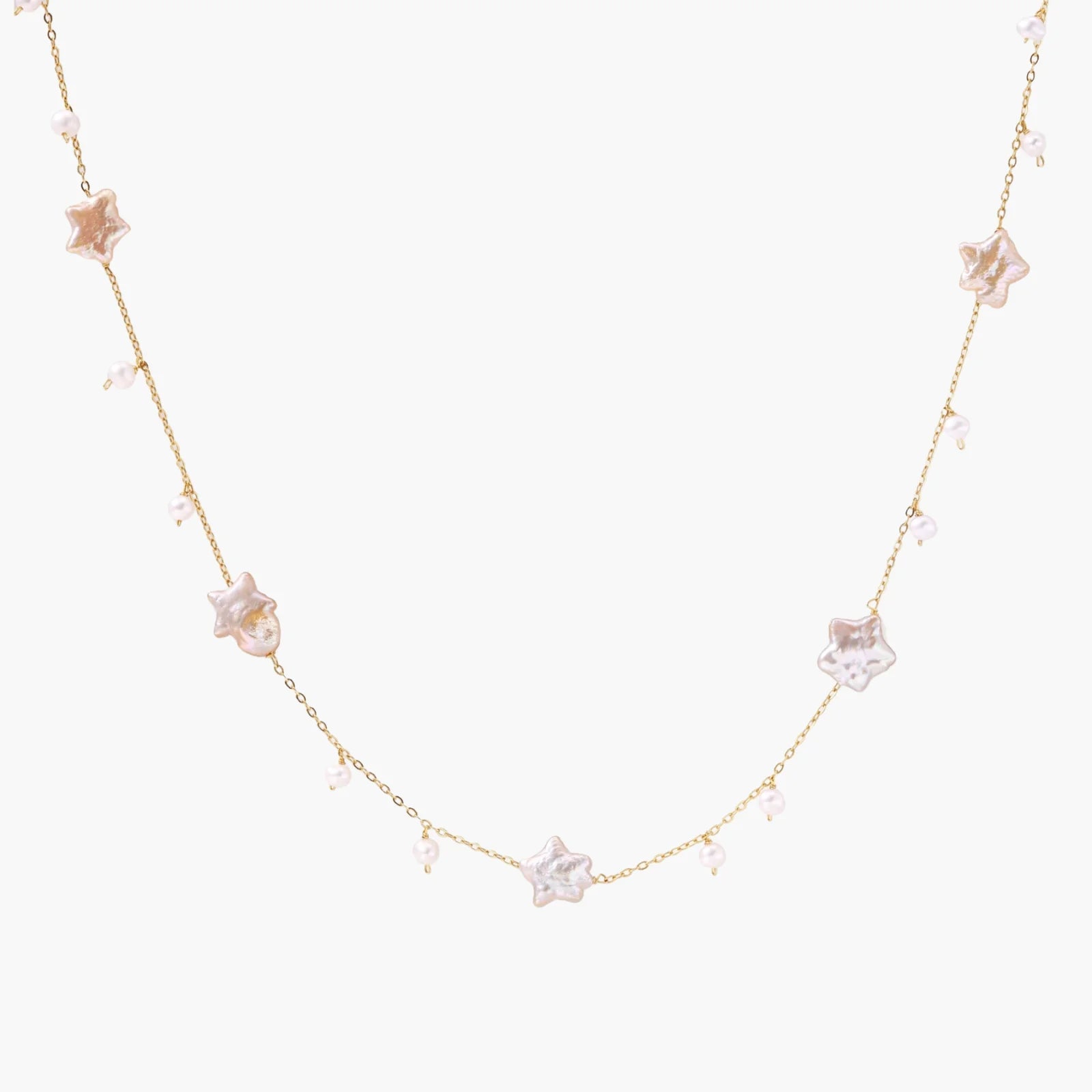 Gold vermeil chain with iridescent star-shaped baroque pearls and small round freshwater pearl drops on cream background.
