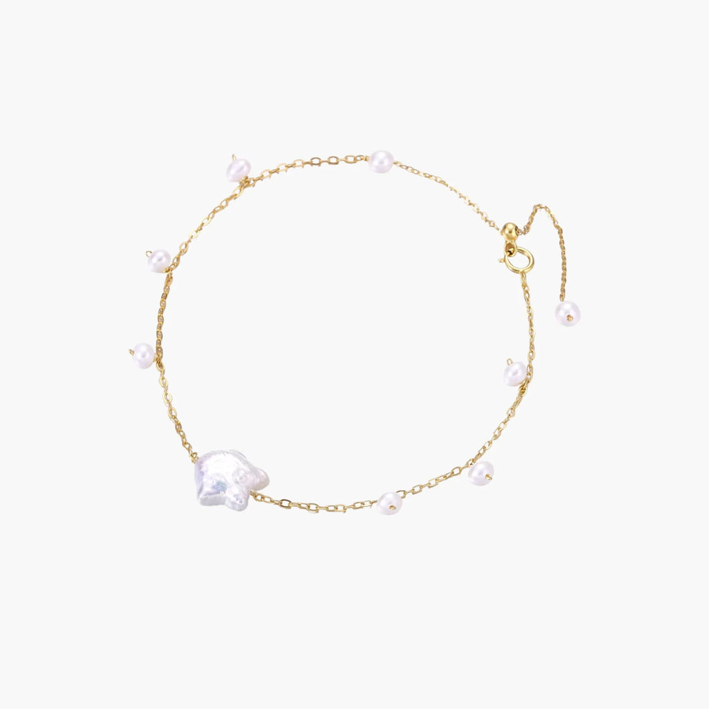 Delicate gold chain bracelet with baroque pearl centerpiece and small freshwater pearls on cream background.