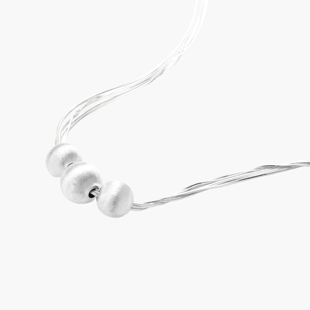 Sterling silver multi-strand necklace with three brushed round beads on cream background